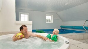 Ein Mann und ein Kind im Whirlpool, im Hintergrund ein Schwimmbad.