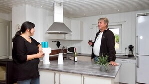 Eine moderne Küche mit weißen Schränken, einer Edelstahl-Dunstabzugshaube und einem eingebauten Backofen. Auf der Arbeitsplatte steht ein kleiner Topfpflanze und eine Weinflasche.