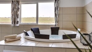Ein modernes Badezimmer mit einer freistehenden Badewanne, einem Handtuchhalter und Blick auf ein grünes Feld durch große Fenster.