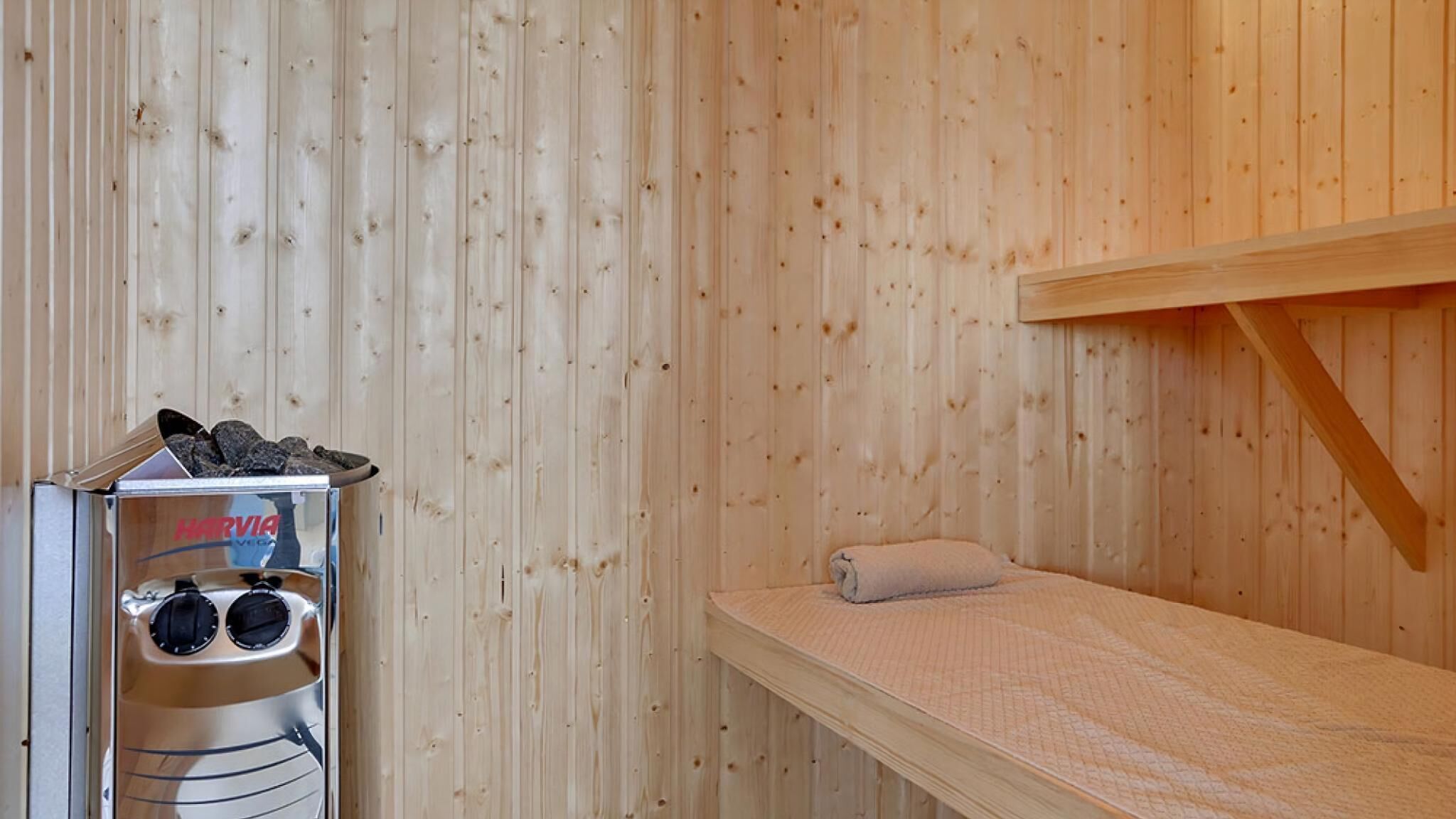A sauna room with a wooden wall, a bench, and a sauna machine labeled "HARVIA".