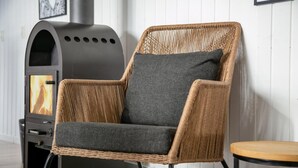 A wicker armchair with a grey cushion, a black outdoor heater, and a small wooden table. - VillaVilla 212 - Marielyst, Lolland/Falster/møn (Idestrup)