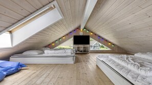 A loft bedroom with a sloped ceiling, wooden flooring, two beds, a flat-screen TV, and a window with a view of a house. - VillaVilla 274 - Tisvildeleje, Nordsjælland (Tisvildeleje)
