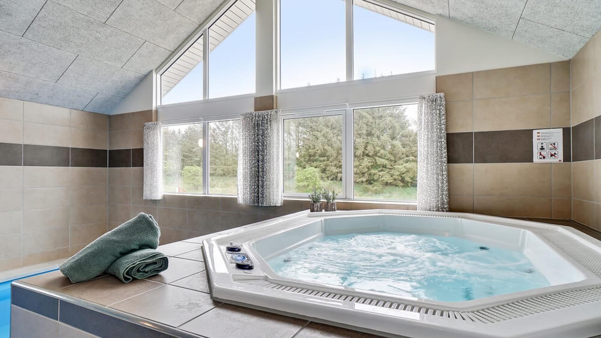 A hot tub in a room with large windows, a towel, and a sign on the wall.
