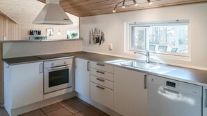 Una cocina moderna con armarios blancos, horno empotrado, lavavajillas y ventana que aporta luz natural.
