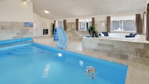 En inomhuspool med en vattenrutschkana, ett bubbelbad och en solterrass med draperier.