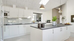 A modern kitchen with white cabinetry, a central island, pendant lighting, and a visible coffee maker. - VillaVilla 491 - Mommark, Sydjylland (Sydals)