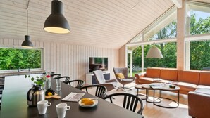 Una sala de estar moderna con techo de madera, ventanas amplias, un sofá y un comedor con mesa y sillas.
