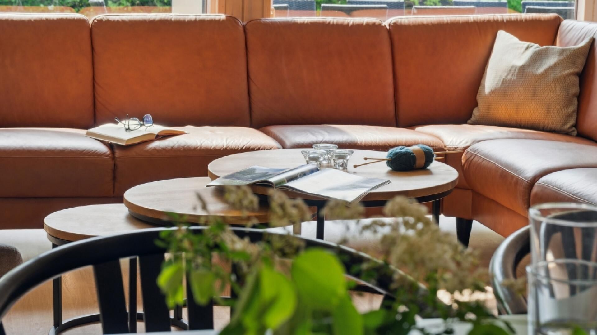 Una sala moderna con un sofá seccional de cuero marrón, una mesa de centro redonda de madera y una mesa de vidrio.