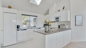 A modern kitchen with white cabinetry, a large island, and a window providing natural light. - VillaVilla 525 - Marielyst, Lolland/Falster/møn (Væggerløse)