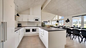 Cozinha moderna com armários brancos, uma ilha central e um espaço de refeições com cadeiras pretas.