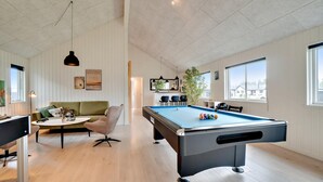 Uma sala de estar moderna com mesa de bilhar, um sofá verde e uma área de refeições com cadeiras.