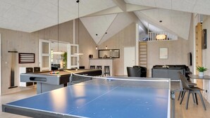 Een ruime kamer met een tafeltennistafel, een pooltafel en een eetgedeelte met hoge plafonds en houten lambrisering.
