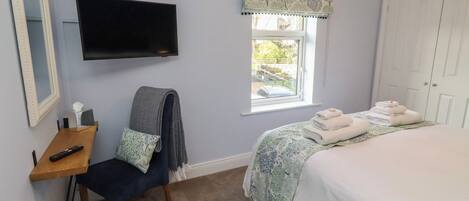 A bedroom with a bed, a TV mounted on the wall, a window with a view of the outside, and a door.