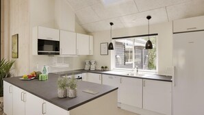 Una cocina moderna con armarios blancos, encimera negra, microondas, cafetera y refrigerador.
