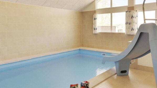 En swimmingpool med en rutsjebane, beige flisevægge og et vindue med gardiner.