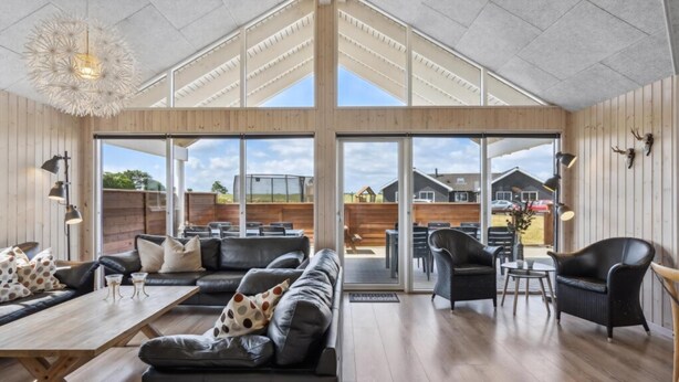 A spacious room with a high ceiling, large windows, and a view of the outside. There is a sofa set, a dining table, and a chair. - VillaVilla 324 - Skåstrup Strand, Fyn og øer (Bogense)
