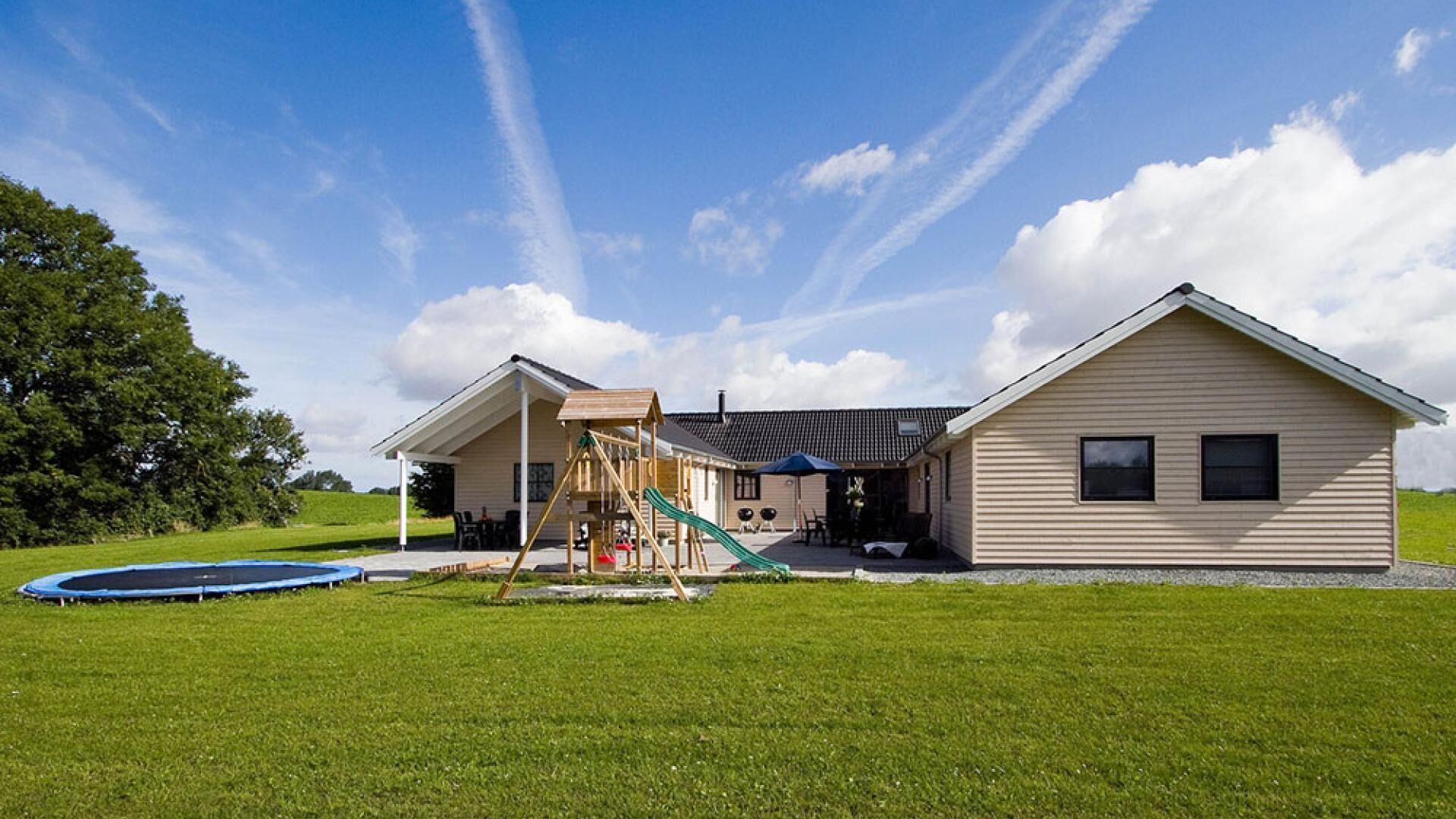 Ein zweistöckiges Haus mit überdachter Terrasse, Trampolin und Spielplatz.