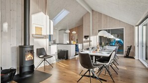 A modern kitchen with a central island, a dining area with a long table and chairs, and a wood-burning stove. - VillaVilla 597 - Rømø, Sydjylland (Rømø)