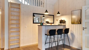 Una cocina moderna con paredes de madera, una barra integrada con tres taburetes negros, un espejo grande sobre la barra y una escalera que lleva a un nivel superior.