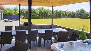 An outdoor patio area with a table and chairs, a hot tub, and a view of a grassy field and trees. - VillaVilla 908 - Marielyst, Lolland/Falster/møn (Væggerløse)