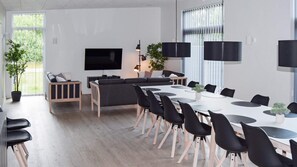 Un salon moderne doté d’un grand téléviseur à écran plat, d’un canapé gris et d’un coin repas avec une table blanche et des chaises noires.