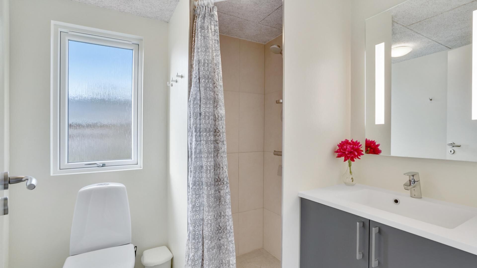 Un bagno con un water, una doccia, un lavandino con uno specchio e una finestra vista su un paesaggio innevato.