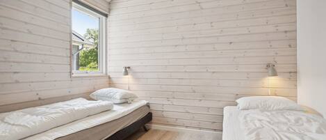 Une chambre avec deux lits simples, des murs en bois, une fenêtre et deux lampes fixées au mur.