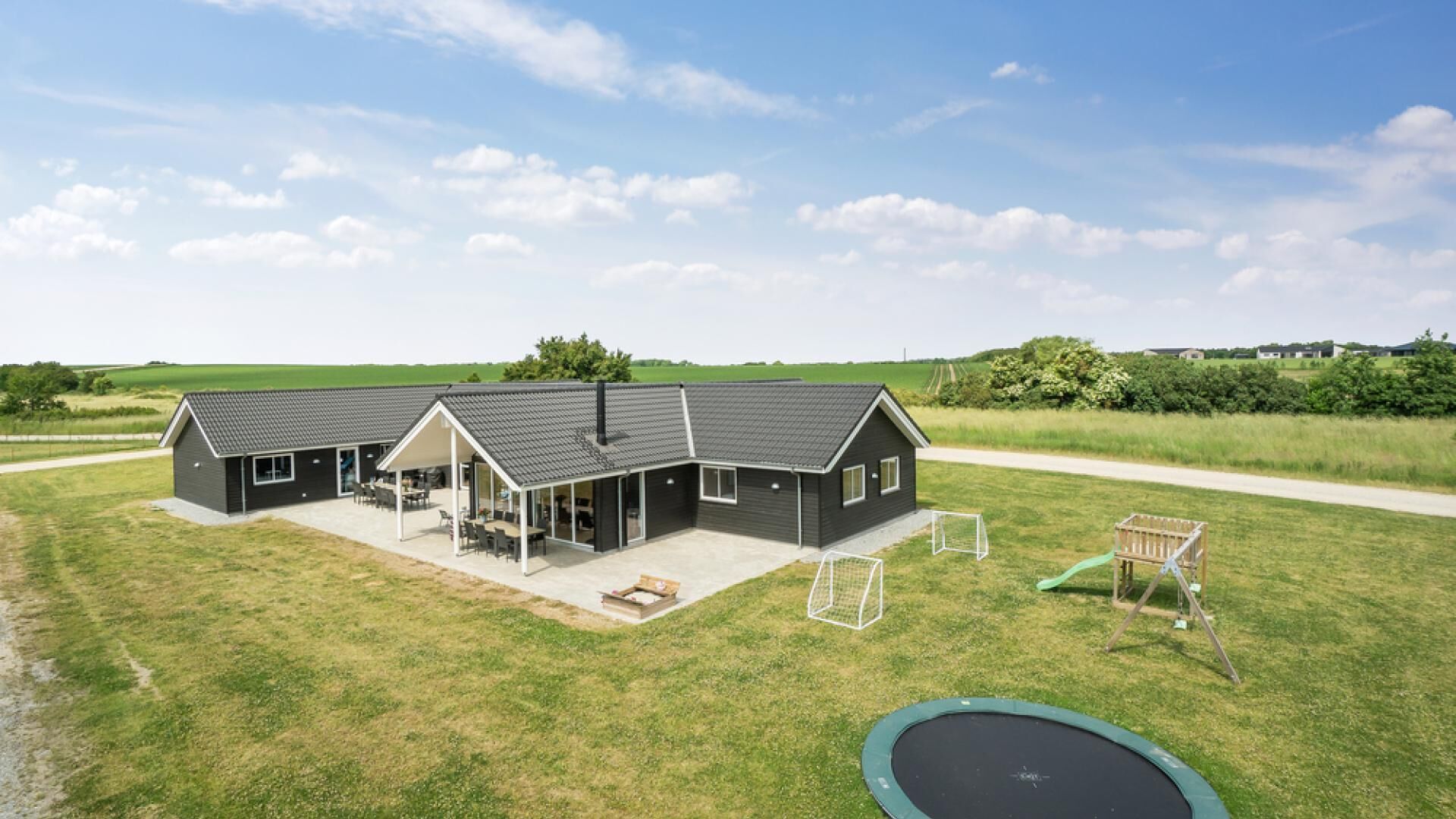 A modern two-story house with a covered patio and a trampoline in the yard.