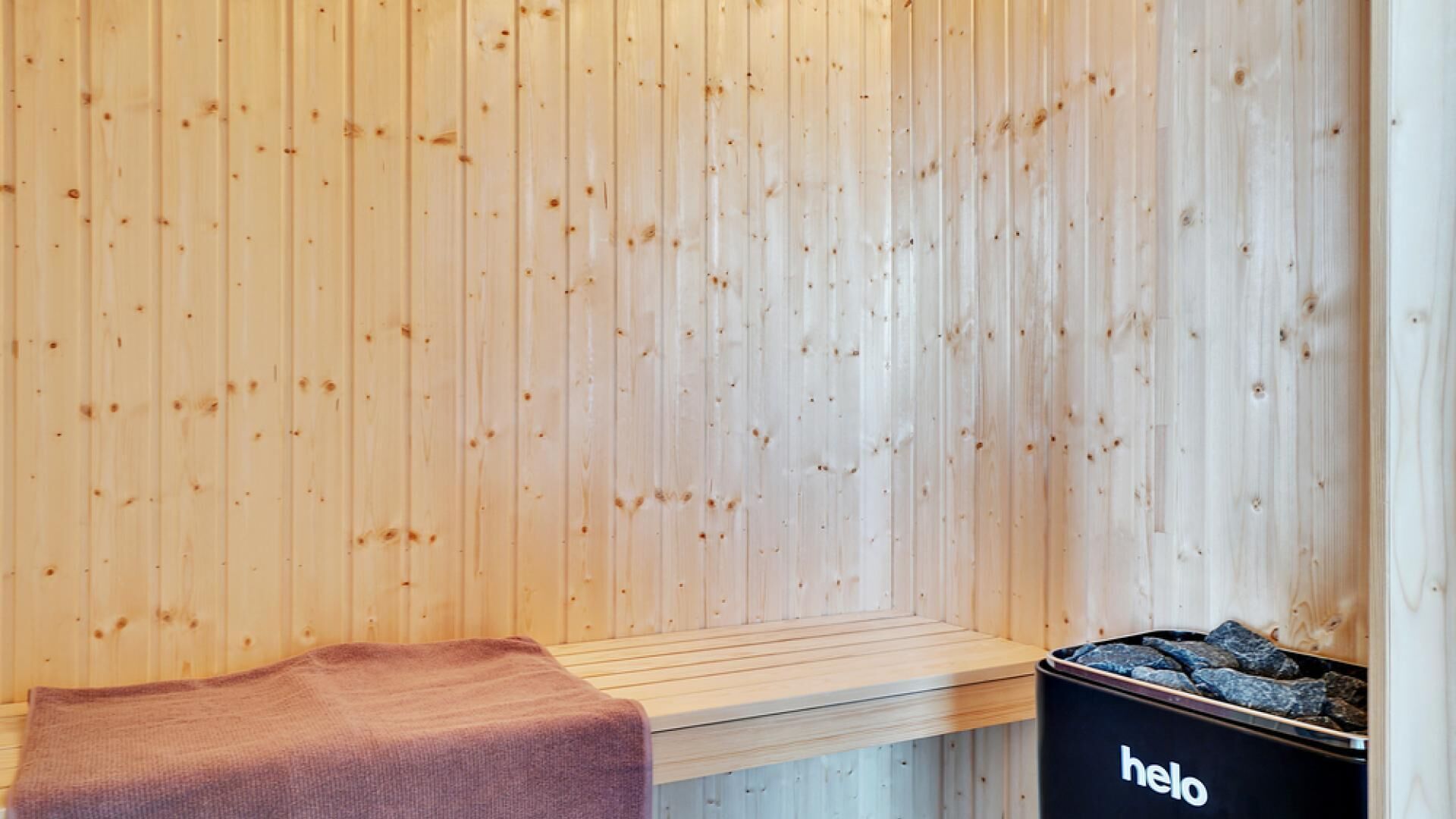 A sauna room with wooden walls, a bench, and a black container labeled "hello" with stones.