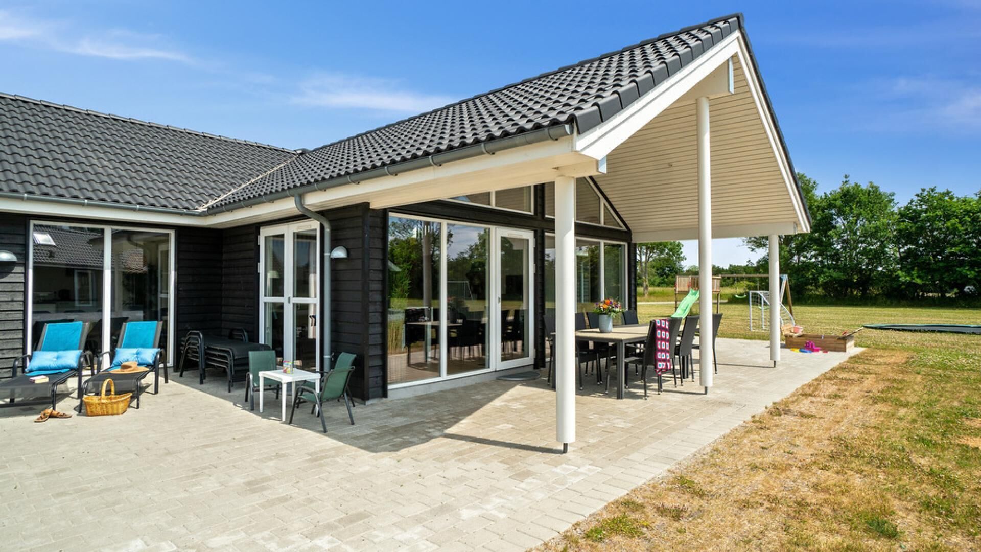 Una casa moderna con un porche cubierto, amplias puertas correderas de vidrio y mobiliario exterior.