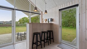 Et moderne udendørs barområde med trævægge, tre sorte barstole og hængende lamper.