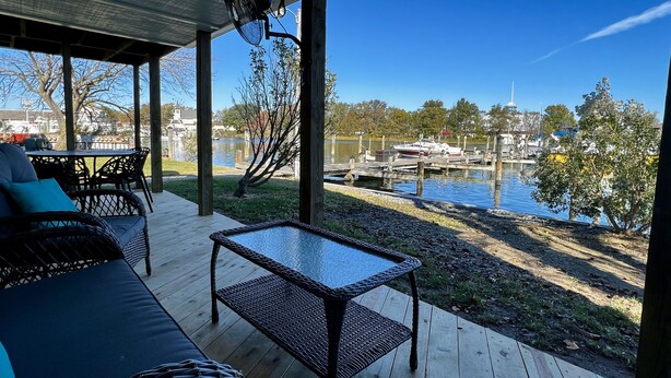 A covered outdoor seating area with a table and chairs, overlooking a body of water and docked boats.