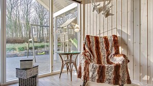 Ein Zimmer mit einem großen Fenster, einem Sessel mit gemustertem Bezug, einem Glastisch und einer Hängelampe.
