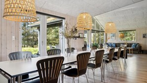 Un vaste espace dédié à la salle à manger, avec une longue table, de nombreuses chaises et des luminaires suspendus.