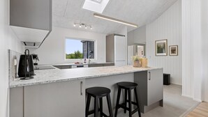 Een moderne keuken met een groot eiland, barstoelen, een koffieapparaat en uitzicht op groen.