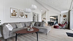 Una sala de estar moderna con un sofá seccional gris, una mesa de centro redonda y un comedor con una mesa y sillas.