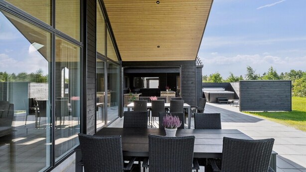 Een modern buitenontbijtgedeelte met een tafel, stoelen, een jacuzzi en een houten terras.