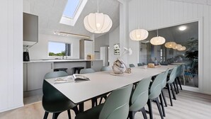 Een moderne keuken met dakraam, een eethoek met een lange tafel en stoelen, en hanglampen.