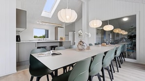 Una cocina moderna con tragaluz, un comedor con una mesa larga y sillas, y lámparas colgantes.