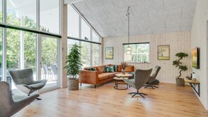 A spacious living room with a large window, a wooden floor, and a modern sofa. - VillaVilla 494 - Thorup Strand, Nordjylland (Fjerritslev)
