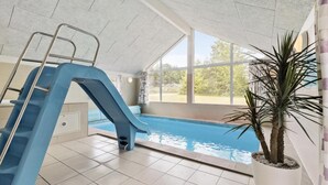 An indoor swimming pool with a blue slide, a ladder, and a large window offering a view of the outdoors. - VillaVilla 380 - Fjellerup, Østjylland (Glesborg)