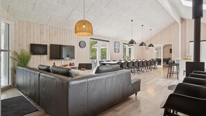 A modern living room with a large L-shaped sectional sofa, a flat-screen TV, and a dining area with a long table and chairs. - VillaVilla 387 - Henne Strand, Vestjylland (Henne)