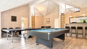 A pool table in a room with wooden walls and a high ceiling. There are chairs and a table with a pool cue rack. - VillaVilla 387 - Henne Strand, Vestjylland (Henne)