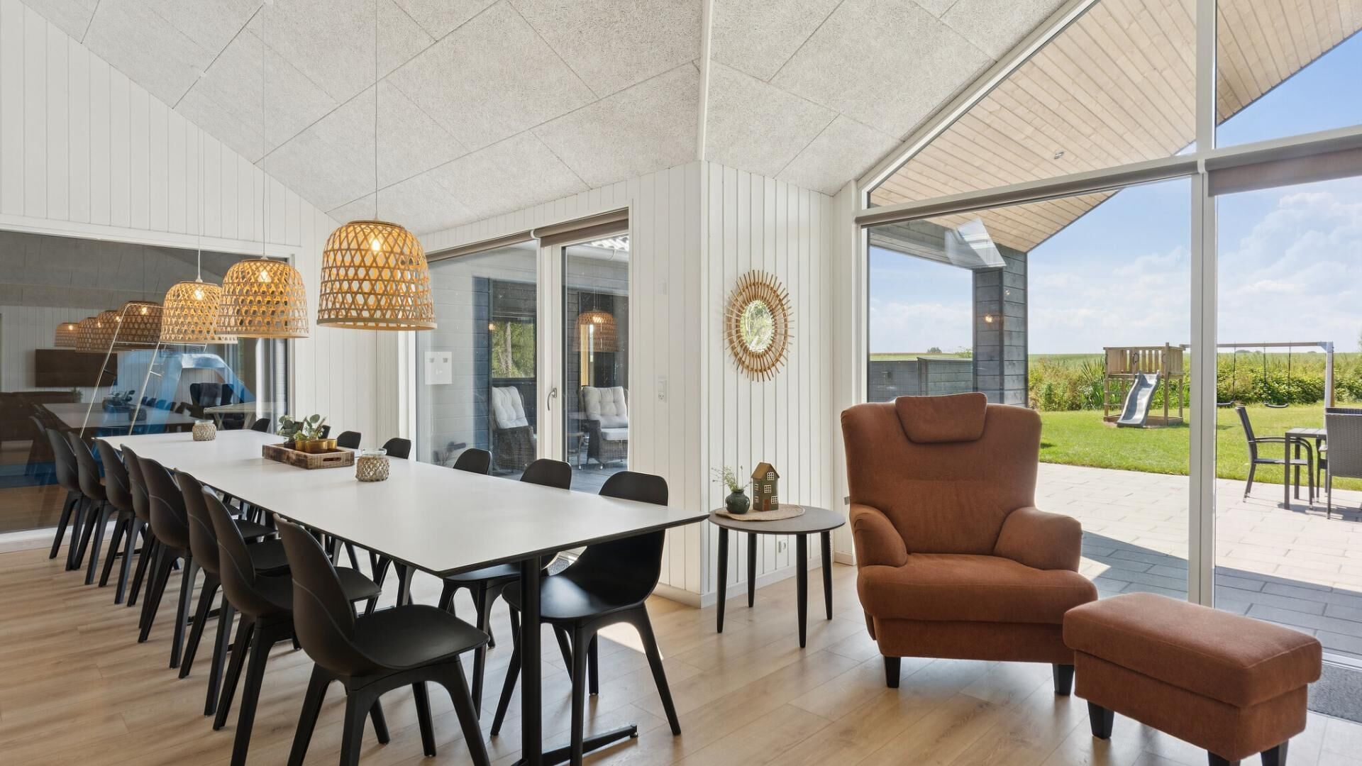 A spacious dining area with a long table, black chairs, and hanging wicker lamps.