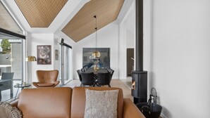 A modern living room with a leather sofa, a dining table with chairs, a fireplace, and a large window. - VillaVilla 584 - Hornbæk, Nordsjælland (Dronningmølle)