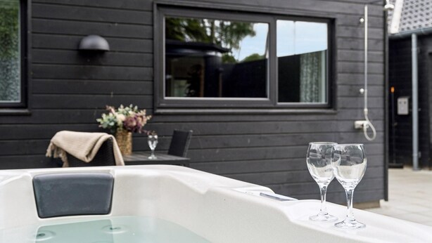A modern outdoor seating area with a table and chairs, a hot tub, and two empty wine glasses. - VillaVilla 584 - Hornbæk, Nordsjælland (Dronningmølle)