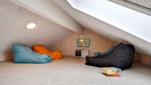 A cozy attic room with a sloped ceiling, a television mounted on the wall, and a small kitchenette area.