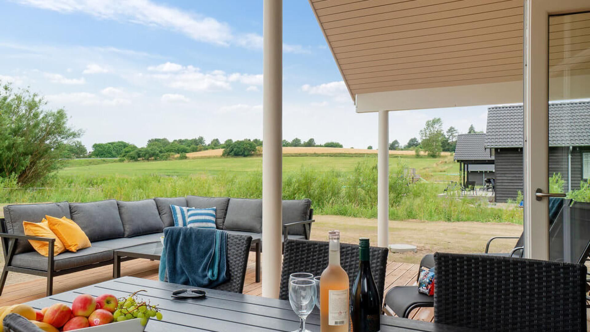 Un espace extérieur aménagé avec un canapé, des chaises et une table sur laquelle sont disposés des fruits et des boissons.