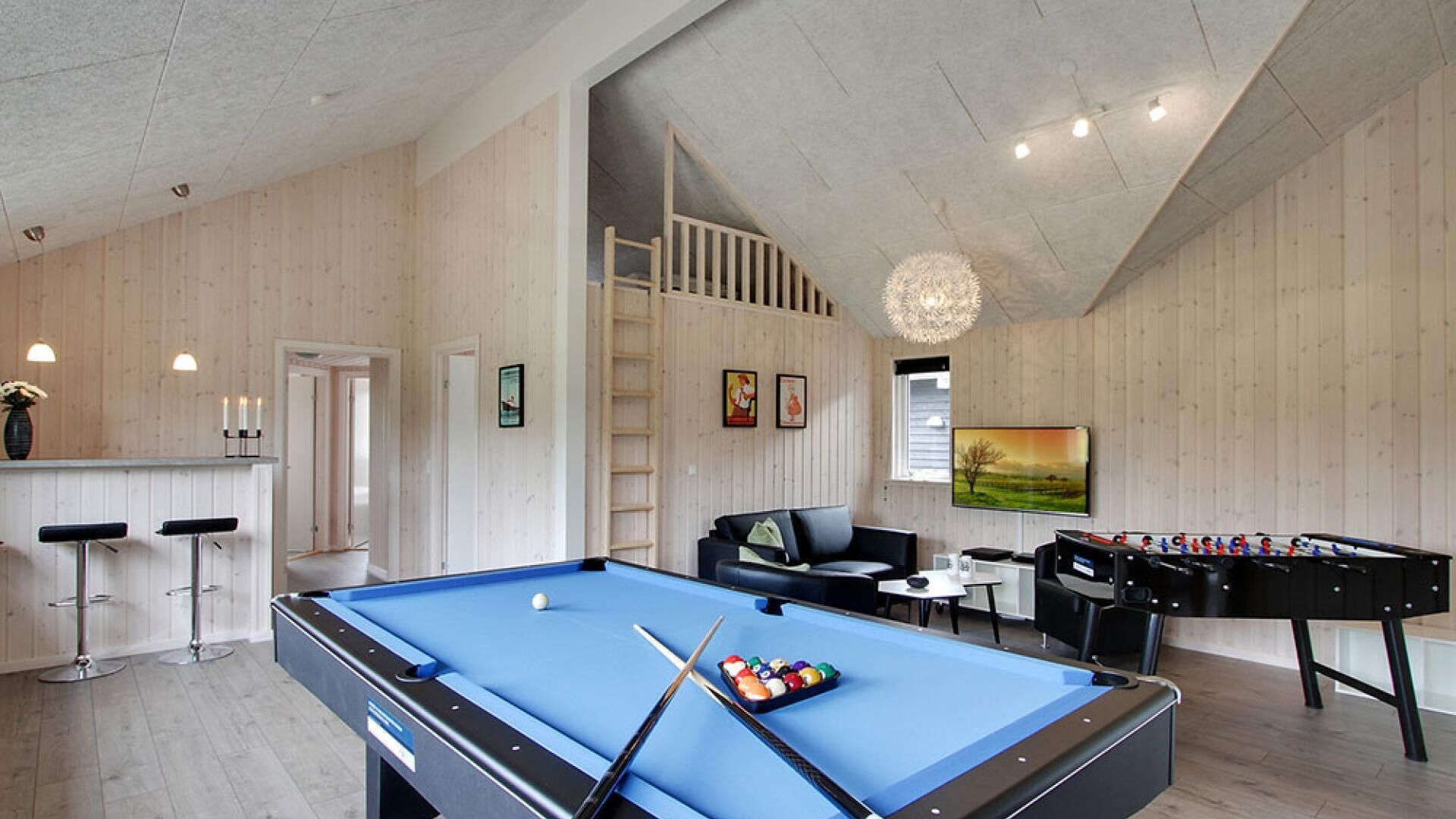 Un espace de loisirs intérieur moderne, doté d’une table de billard, d’un baby-foot et d’un coin salon confortable.