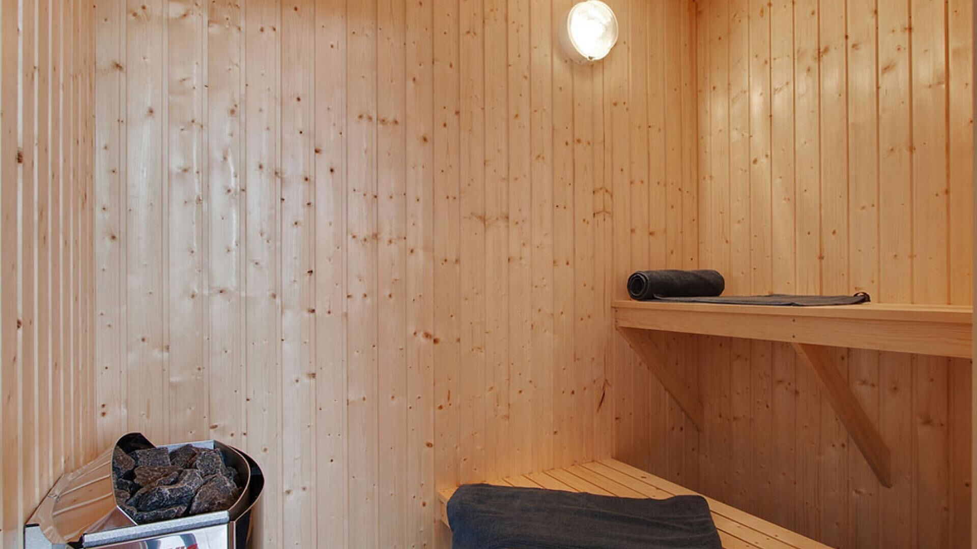 A sauna room with wooden walls, a bench, a shelf, and a heater.